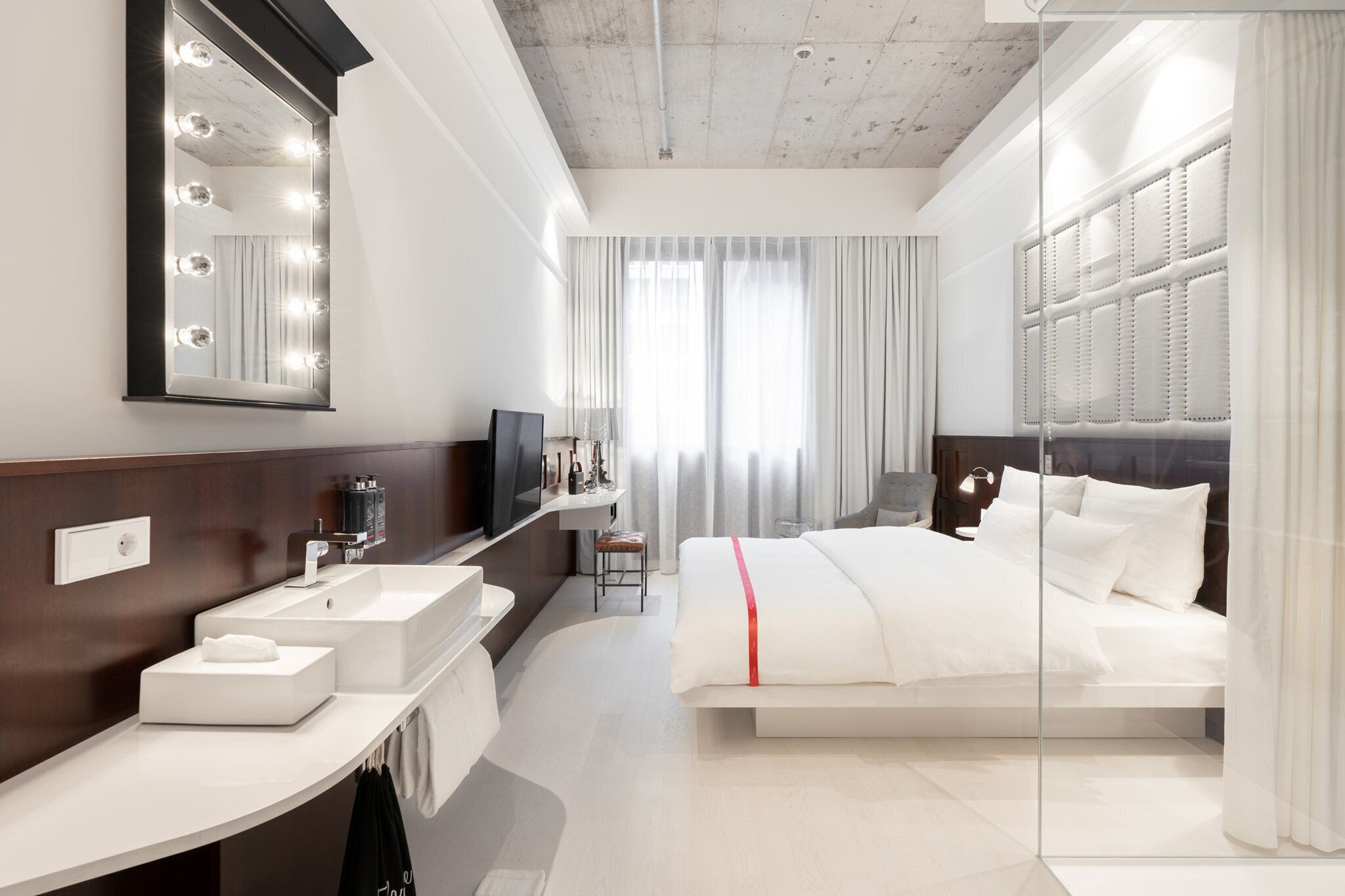 A modern hotel room with a large mirror, a bed, a vanity with a sink, and a television.