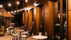 An outdoor patio area with tables and chairs, string lights, and a building with large windows. - Ruby Louise Hotel Frankfurt by IHG (Frankfurt)