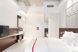 A modern hotel room with a large bed, a vanity with a mirror and lights, a television, and a bathroom visible through an open door. - Ruby Louise Hotel Frankfurt by IHG (Frankfurt)