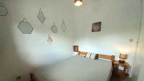 Ein Schlafzimmer mit Bett, Holz-Kopfteil, Nachttisch mit Lampe und geometrischer Wandkunst.