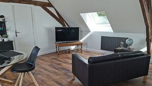 Ett modernt sovrum i loftstil med ett sluttande tak, trägolv, en svart lädersoffa, ett glasbord och en tv som står på ett träställ.