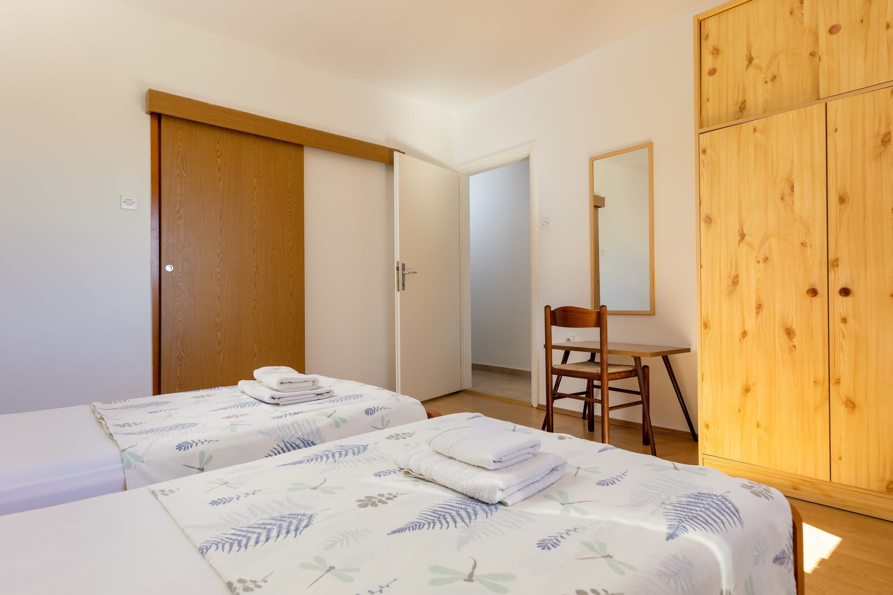 Ett hotellrum med två sängar, en garderob i trä, ett skrivbord och en stol.