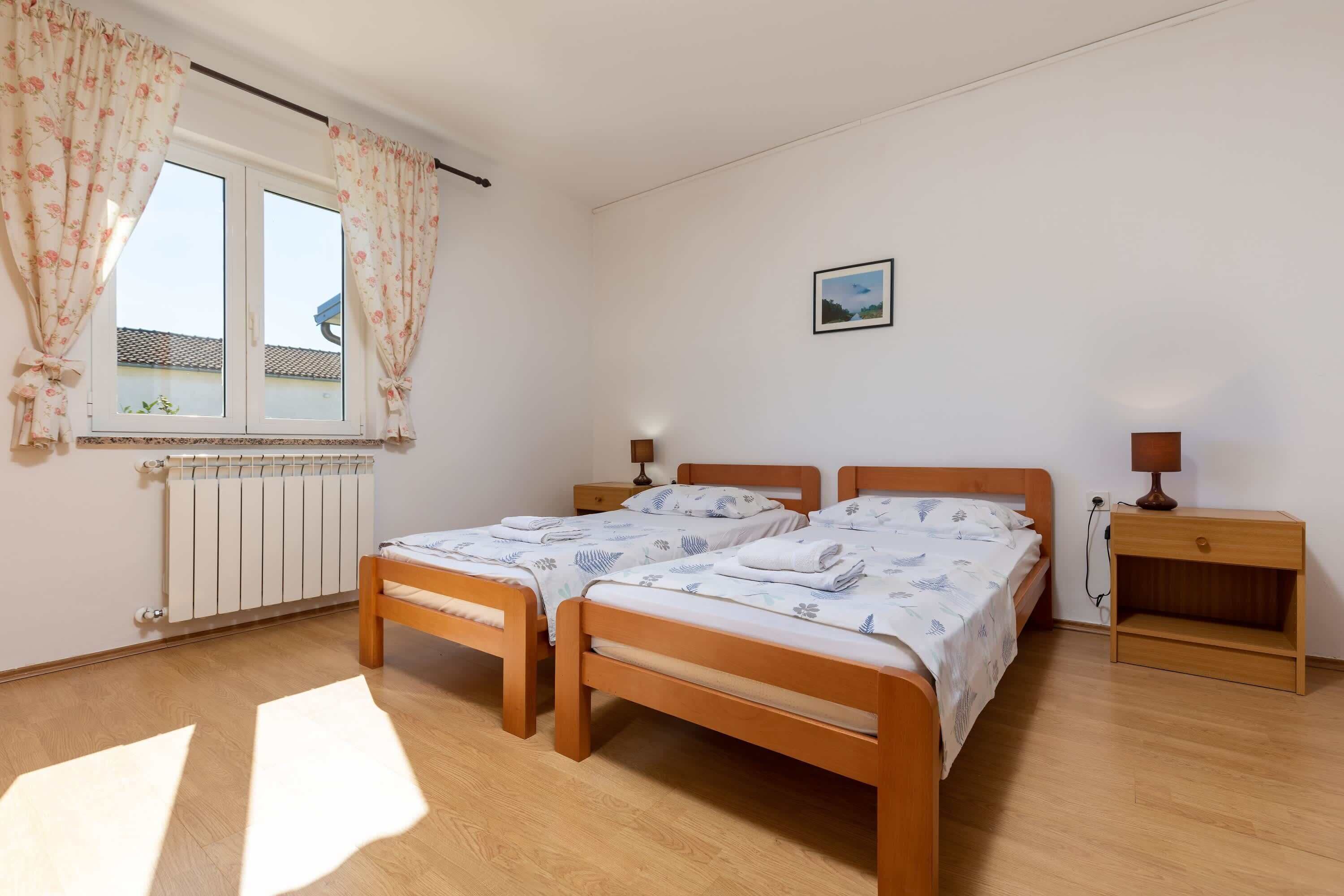 A bedroom with two wooden beds, a bedside table with a lamp, a radiator, and a window with curtains.