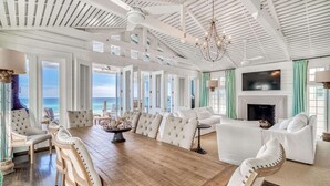 A spacious room with a large wooden dining table, white upholstered chairs, a fireplace, and a view of the ocean. - Gulf Front in the Middle of Seaside! Elevator, Community Pools, Bikes, and More (Santa Rosa Beach)