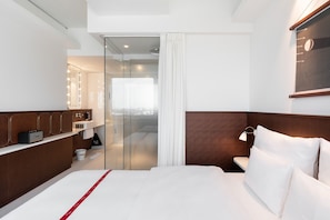A modern hotel room with a bed, a vanity with a mirror, a shower area, and a view through a glass door. - Ruby Luna Hotel Dusseldorf by IHG (Düsseldorf)