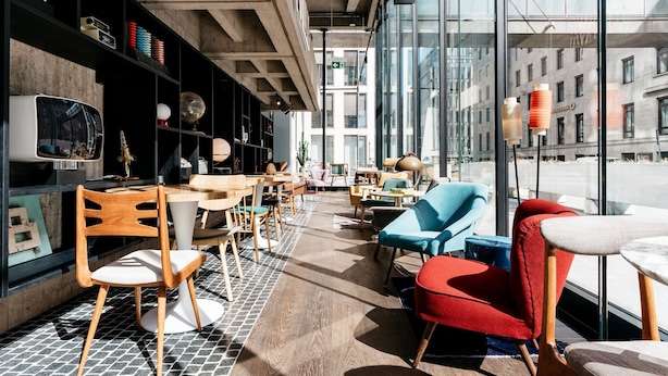 Un interior moderno con piso de madera, mesas, sillas y un ventanal con vistas a la ciudad.