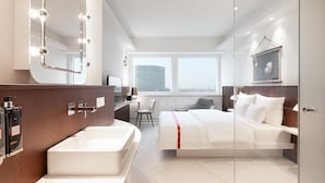 Una habitación de hotel moderna con un espejo grande, una bañera, una cama, un escritorio y una silla.