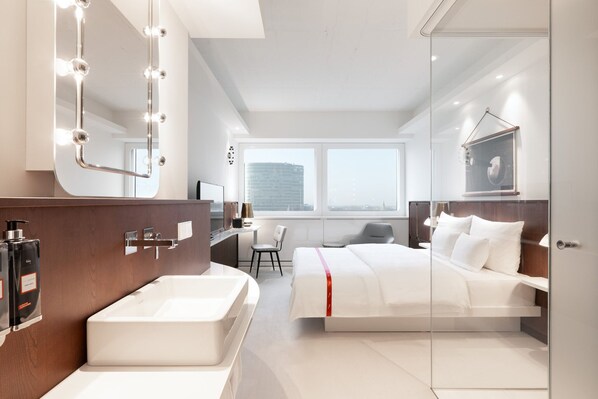 Una habitación de hotel moderna con un espejo grande, una bañera, una cama, un escritorio y una silla.