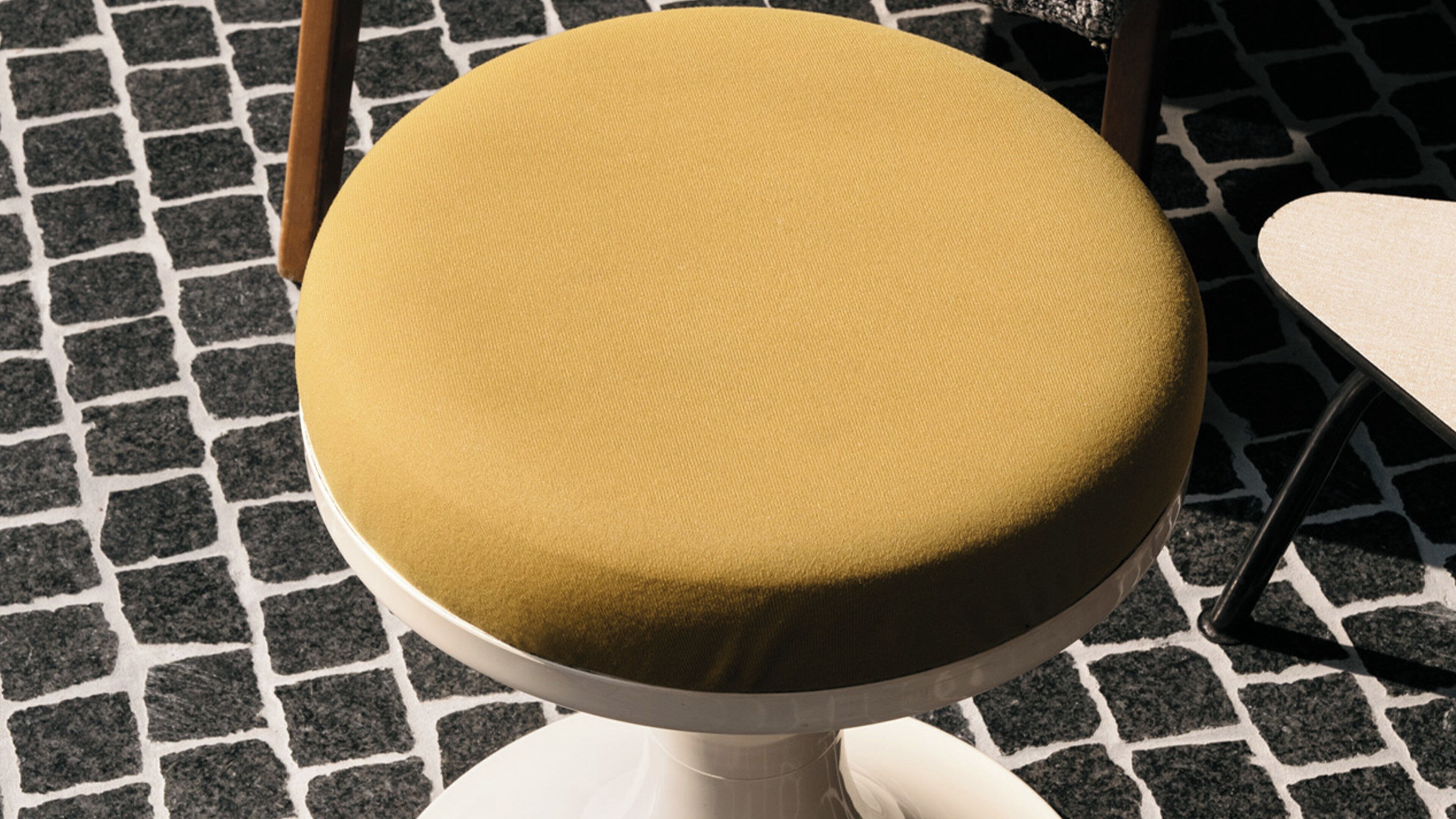 Un tabouret rond de couleur beige, doté d’un siège texturé, posé sur un socle blanc.