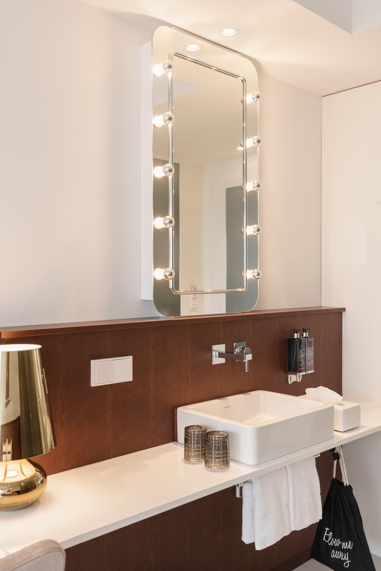 A bathroom with a vanity, a mirror with lights, a sink, and a towel rack.