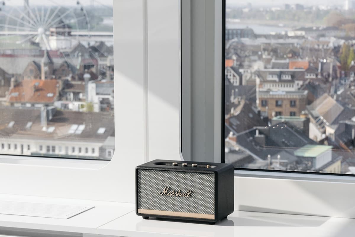 Un altavoz Marshall sobre un alféizar con vistas a un paisaje urbano y una noria.