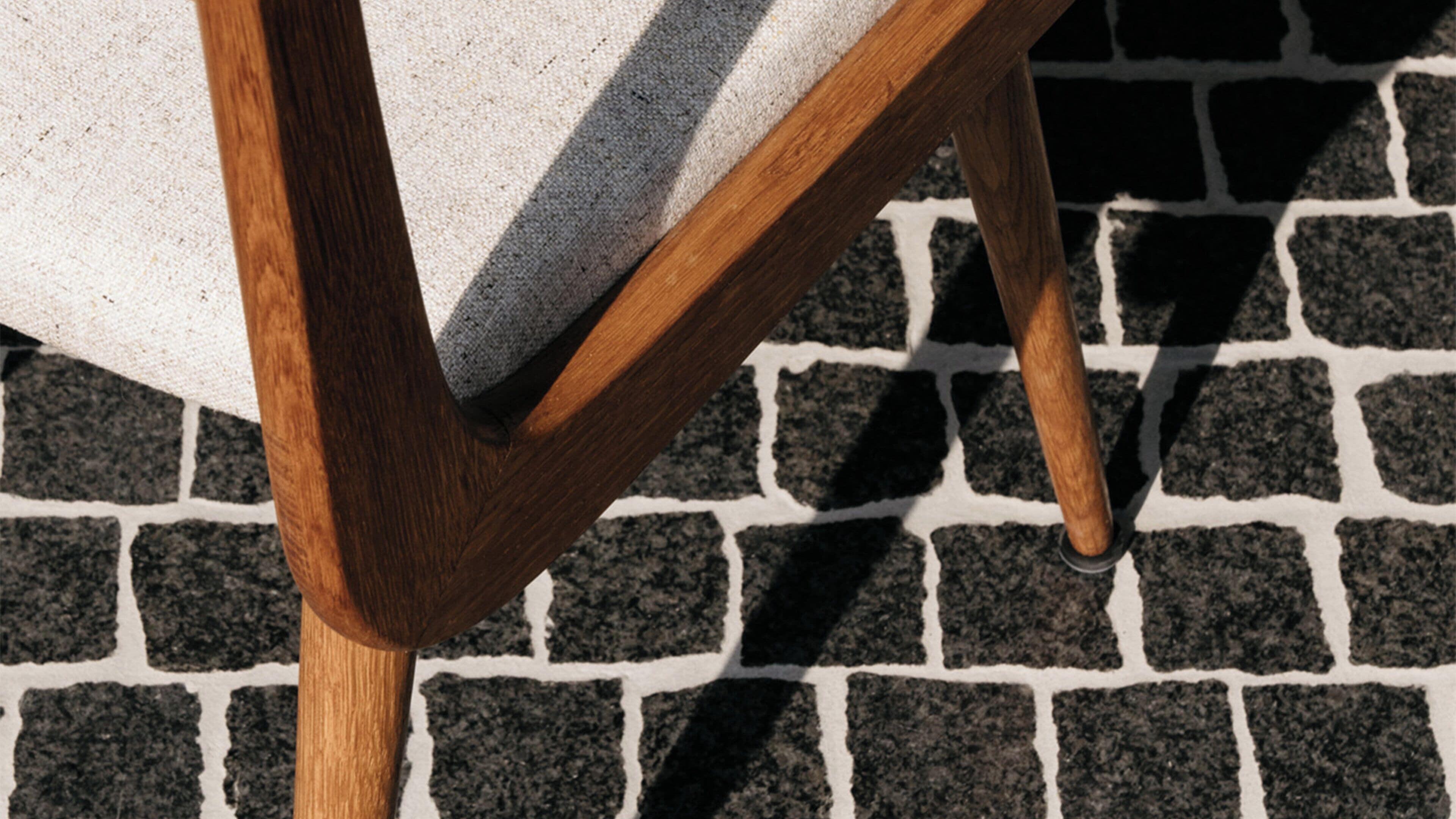 A wooden chair with a grey cushion on a cobblestone floor.