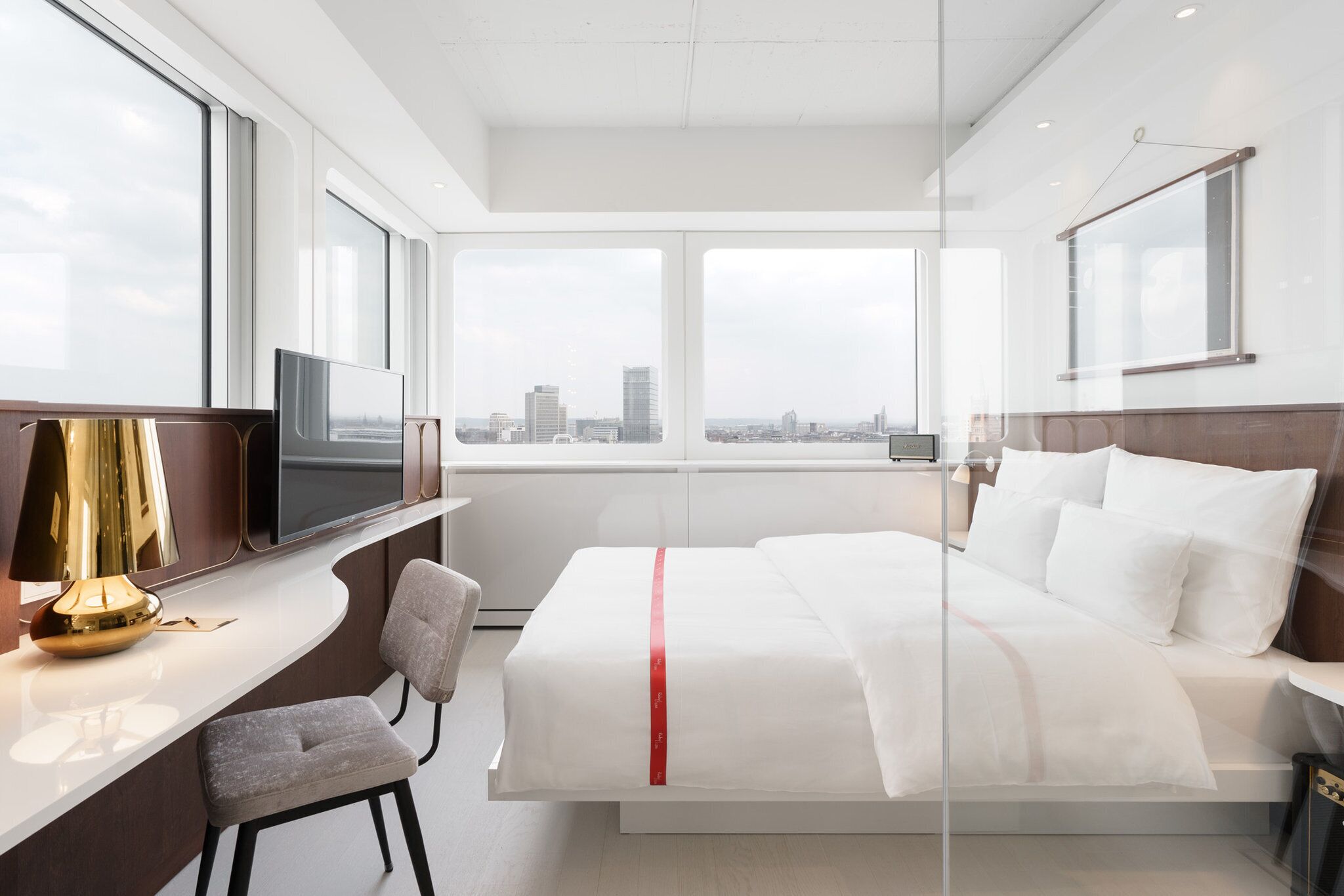 A modern hotel room with a large bed, a desk with a chair, a television, and a city view.