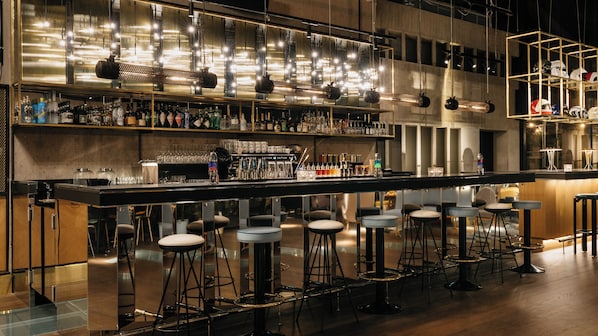 Un espace bar avec des tabourets, un long comptoir et diverses bouteilles et verres.