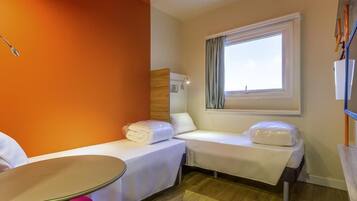 Quarto de hotel com duas camas de solteiro, uma mesa redonda pequena e uma janela com cortinas.