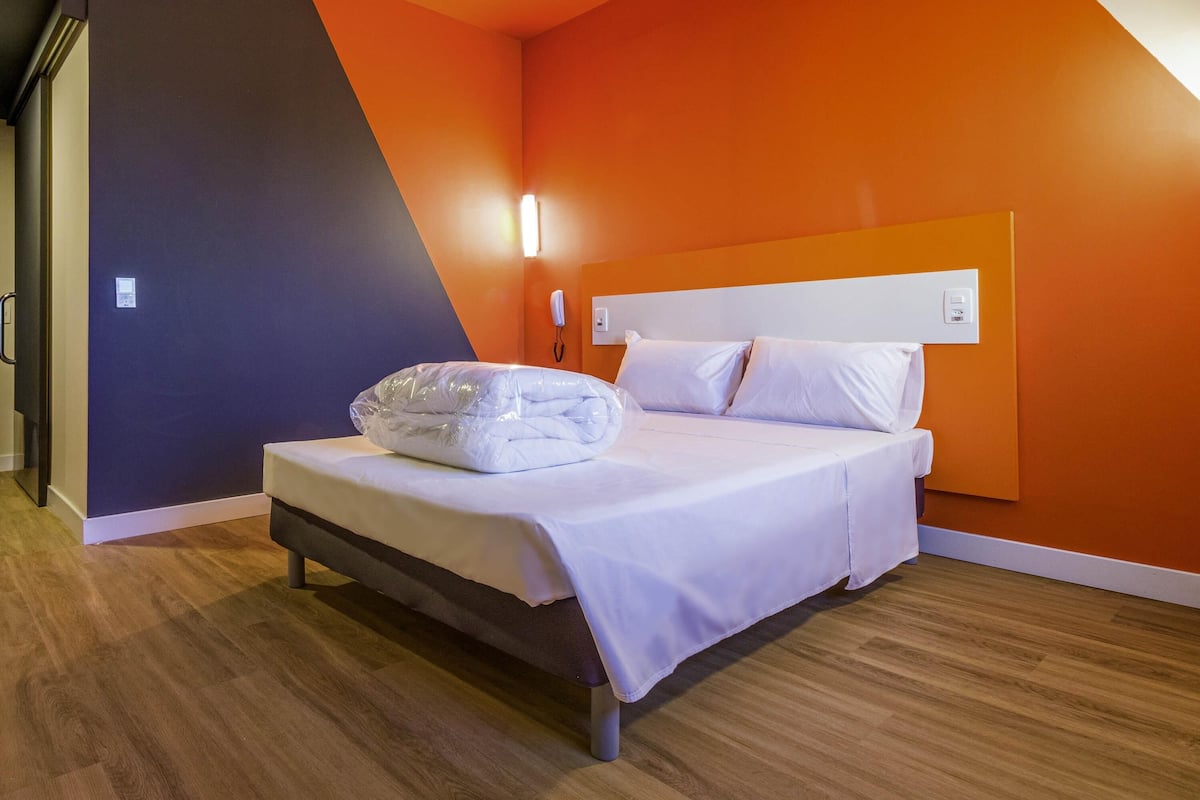 Een hotelkamer met een bed, een telefoon en een wandlamp.