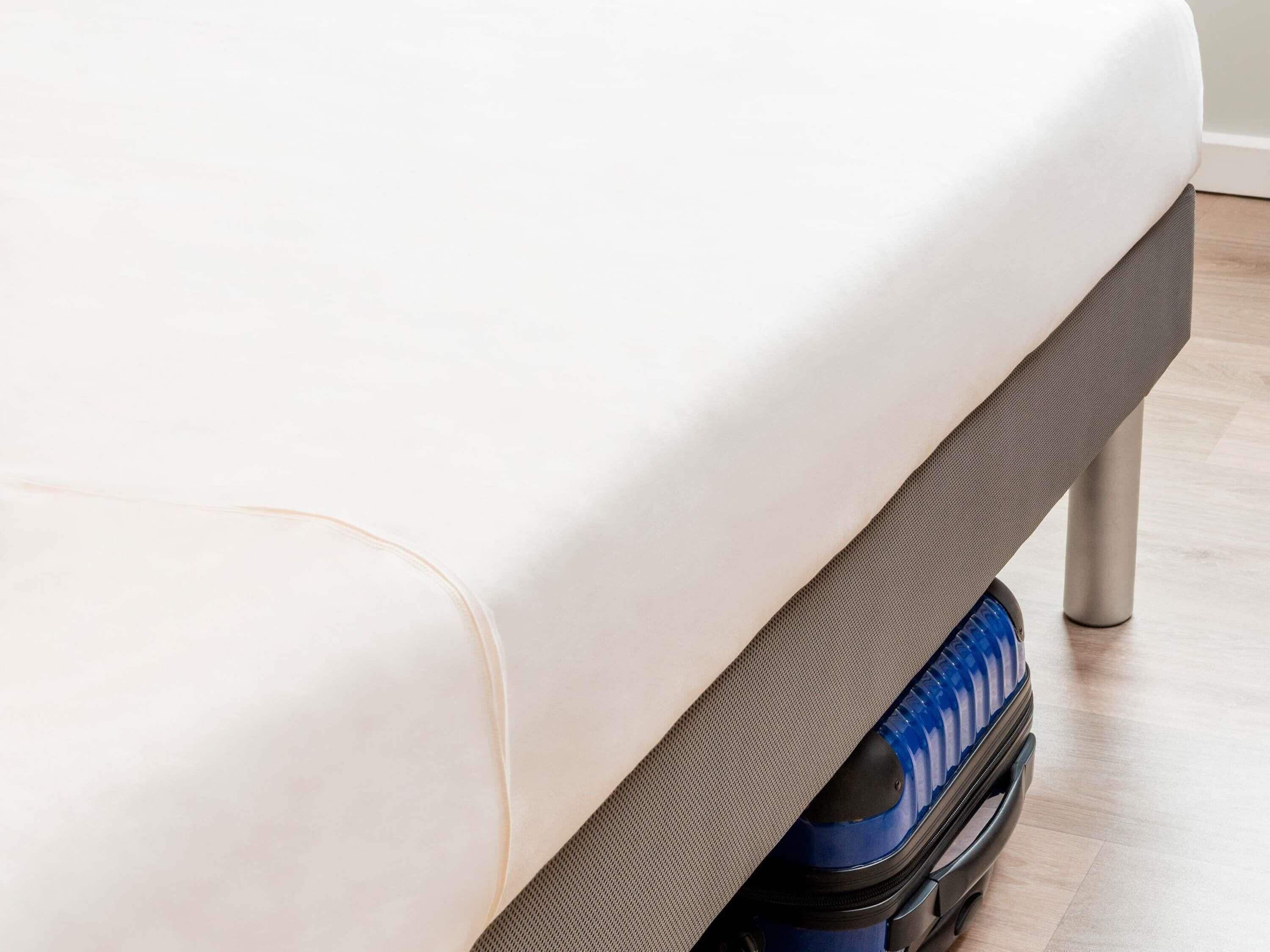 Un lit avec un matelas et un compartiment de rangement situé sous le lit, de couleur grise.