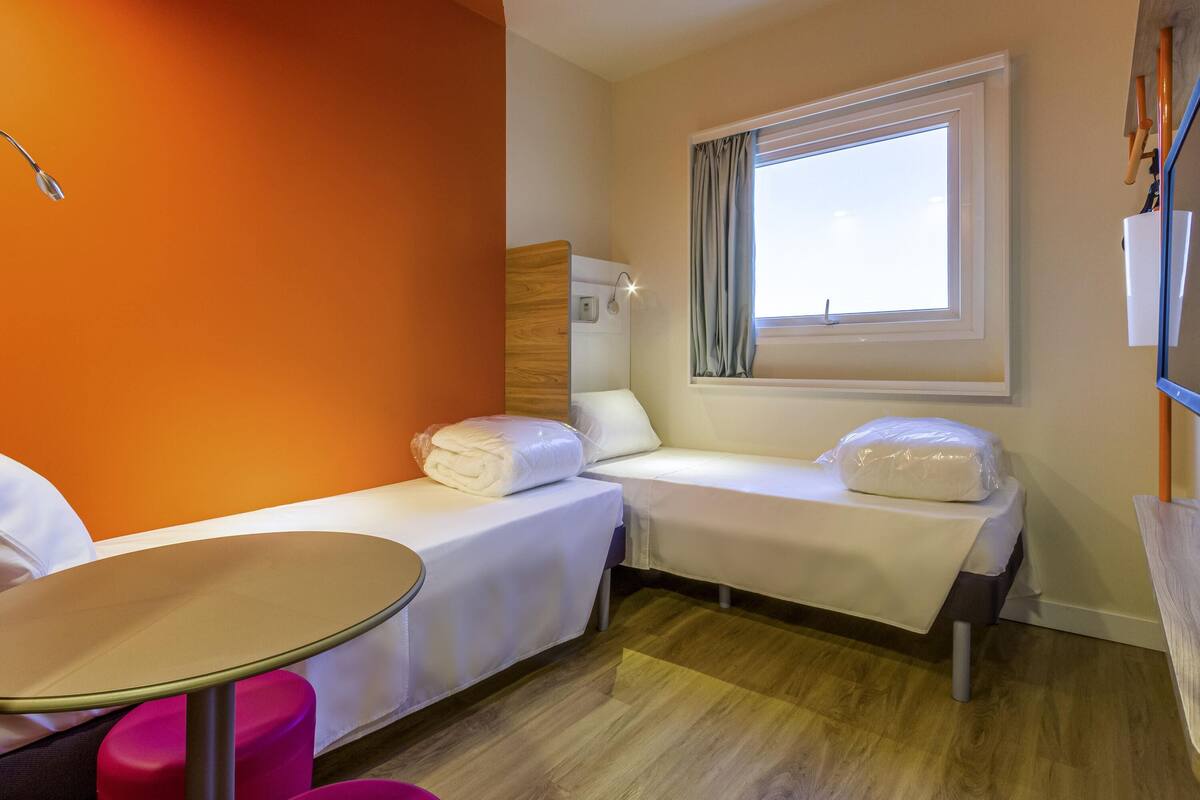 Een hotelkamer met twee bedden, een tafeltje en een raam met gordijnen.