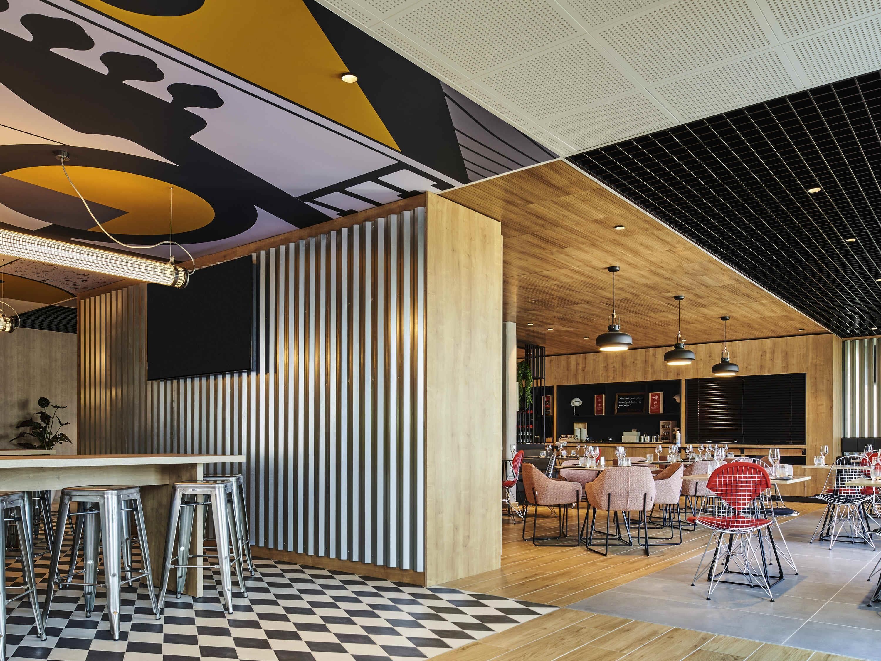 A modern restaurant interior with a checkered floor, bar area with stools, and dining tables with chairs.