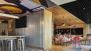 Ein modernes Restaurant mit Schachbrettboden, einer Bar mit Hockern und Esstischen mit Stühlen.
