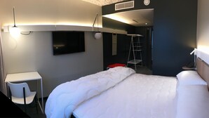 Une chambre d’hôtel avec un lit, un bureau, une chaise, une télévision et une échelle.