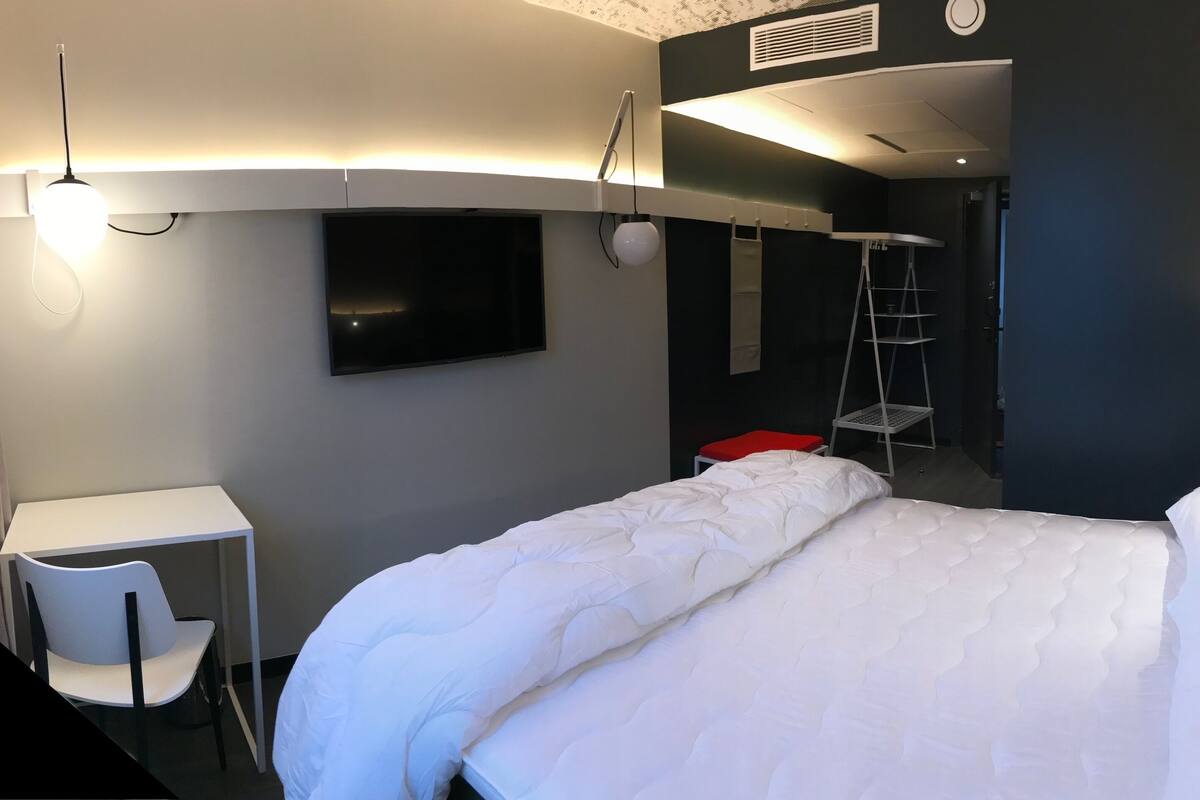 Une chambre d’hôtel avec un lit, un bureau, une chaise, une télévision et une échelle.
