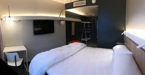 Une chambre d’hôtel avec un lit, un bureau, une chaise, une télévision et une échelle.
