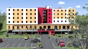 Un hôtel à plusieurs étages, avec une façade centrale rouge et blanche, de nombreux balcons et un parking où sont garées plusieurs voitures.
