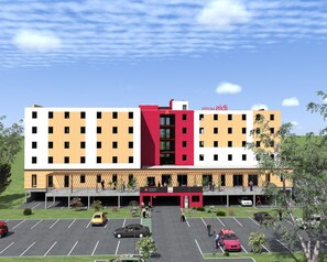 Un hôtel à plusieurs étages, avec une façade centrale rouge et blanche, de nombreux balcons et un parking où sont garées plusieurs voitures.