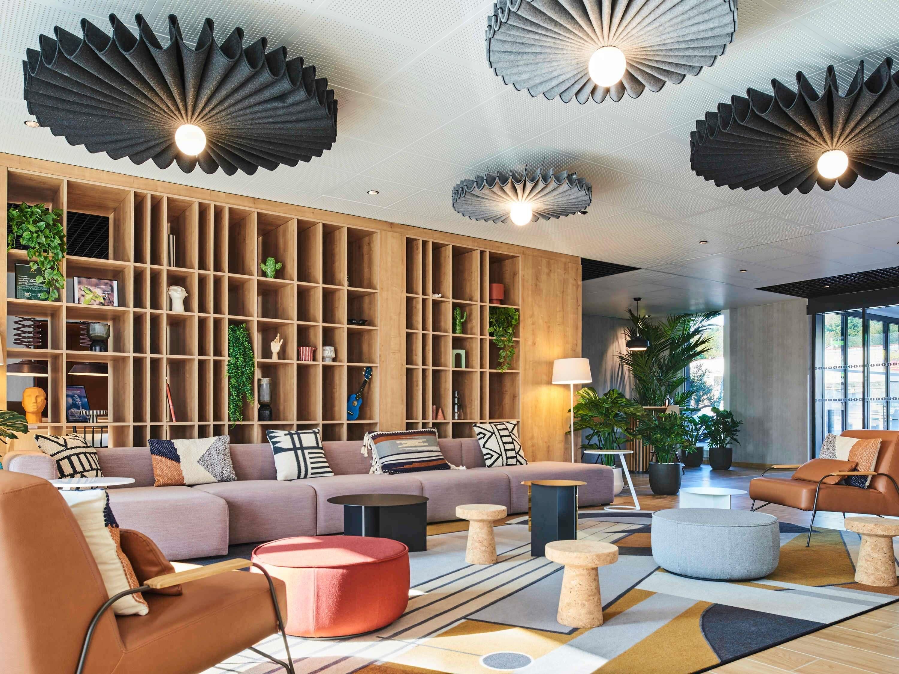 Una sala de estar moderna con un sofá seccional, otomanas redondas, una mesa de centro y un estante de madera lleno de objetos decorativos.