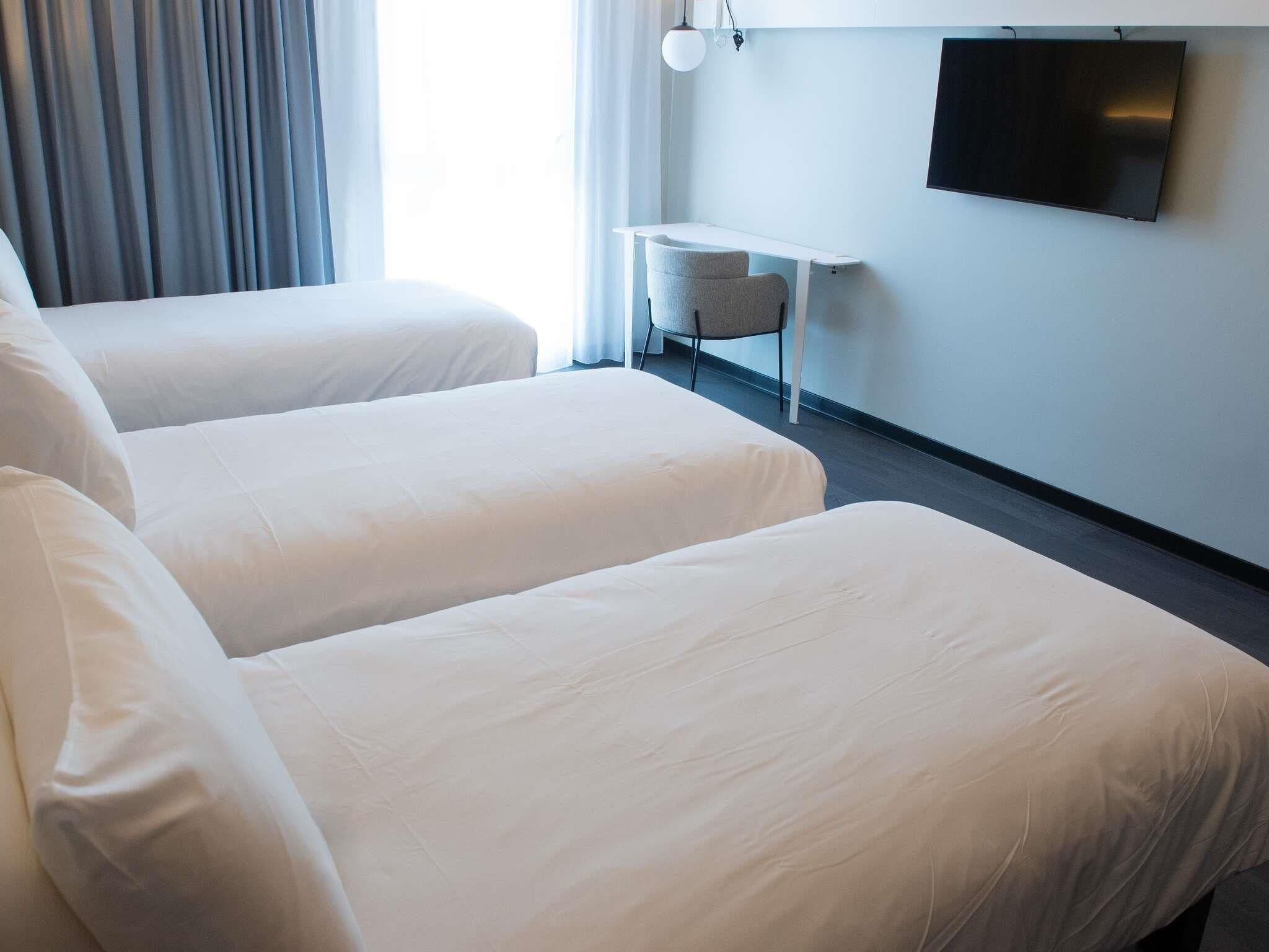 A hotel room with two single beds, a small table, a chair, and a TV mounted on the wall.