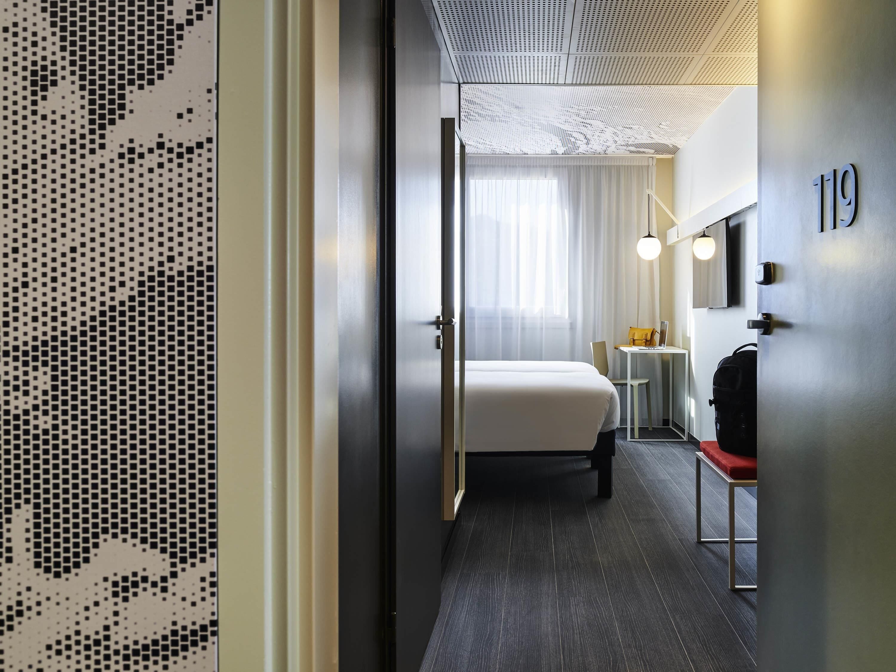 A hotel room with a bed, a desk, a chair, a suitcase, and a number '19' on the wall.