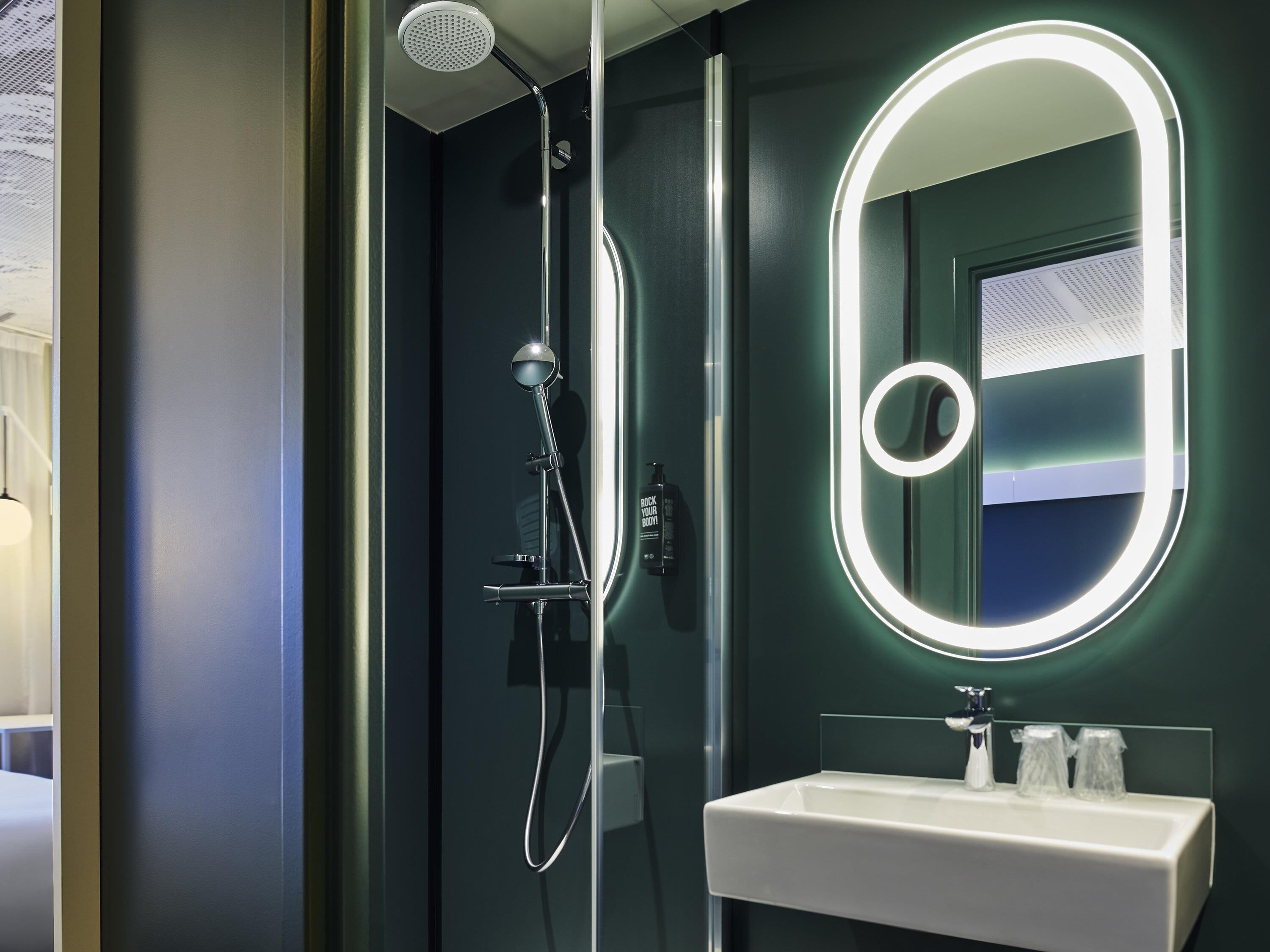 A modern bathroom with a glass-enclosed shower, a white sink with a mirror, and a wall-mounted light.