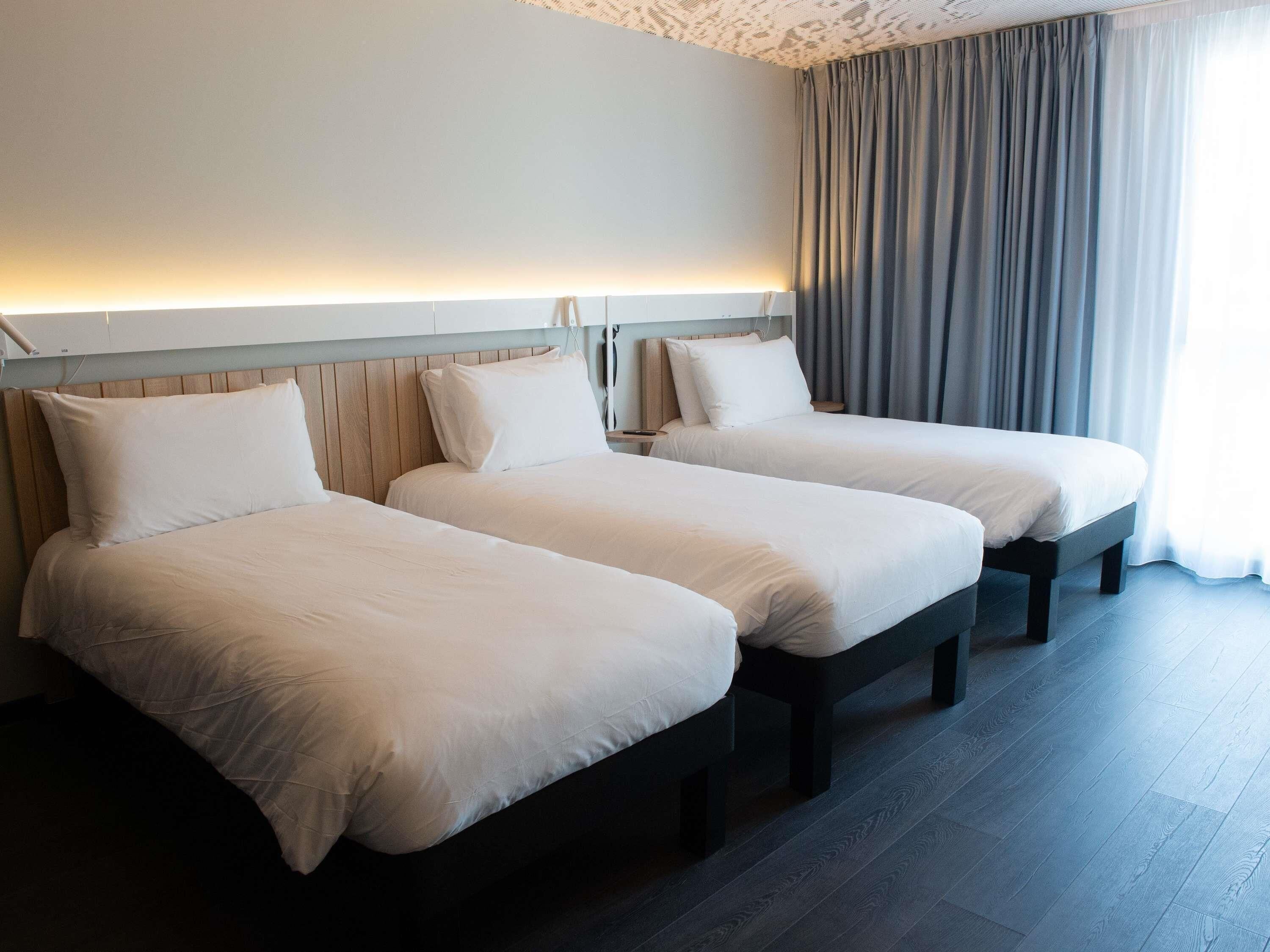 Ein Hotelzimmer mit zwei Betten, einem Holzkopfstück, einem Nachttisch und einem Fenster mit Vorhängen.