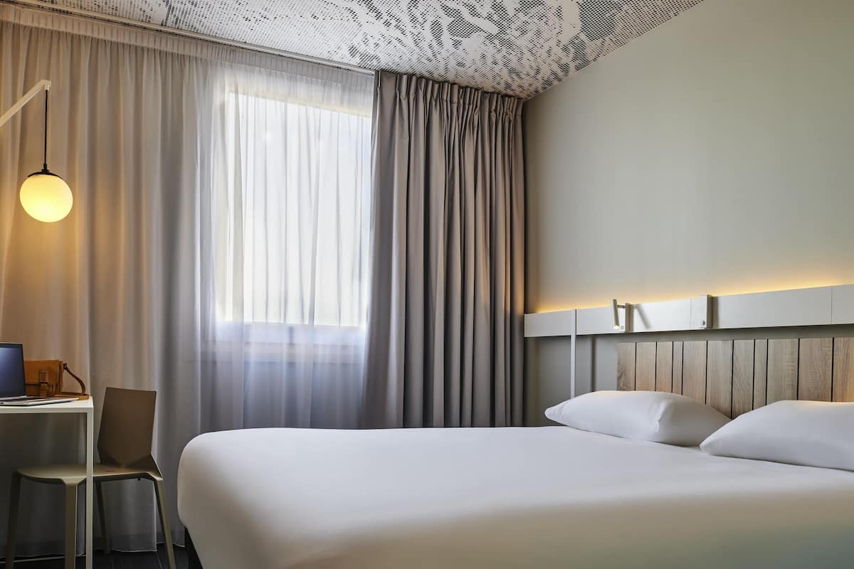 Ein Hotelzimmer mit Bett, Schreibtisch, Stuhl und einem Fenster mit Vorhängen.