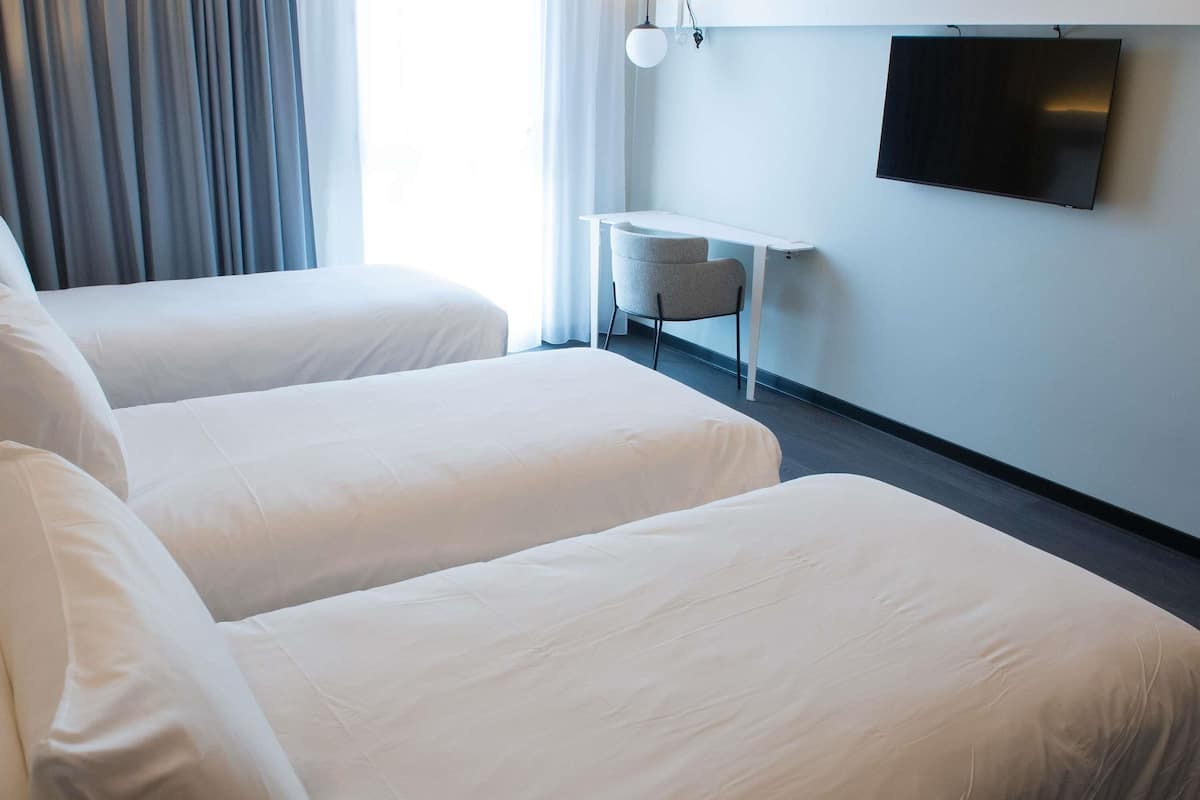 Ein Hotelzimmer mit zwei Betten, einem kleinen Tisch, einem Stuhl und einem an der Wand befestigten Fernseher.