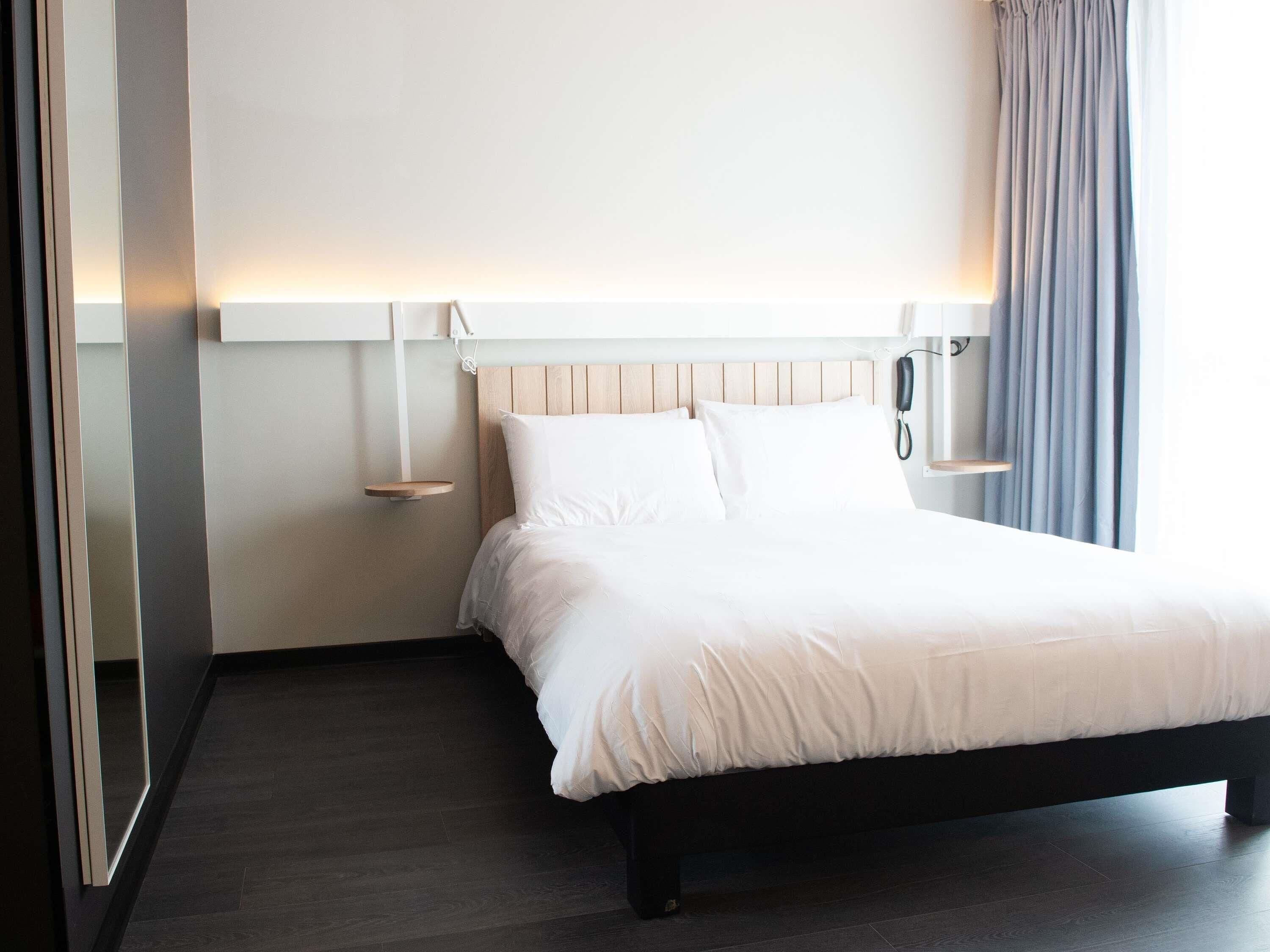 Habitación de hotel con cama, mesitas de noche, teléfono y ventana con cortinas.
