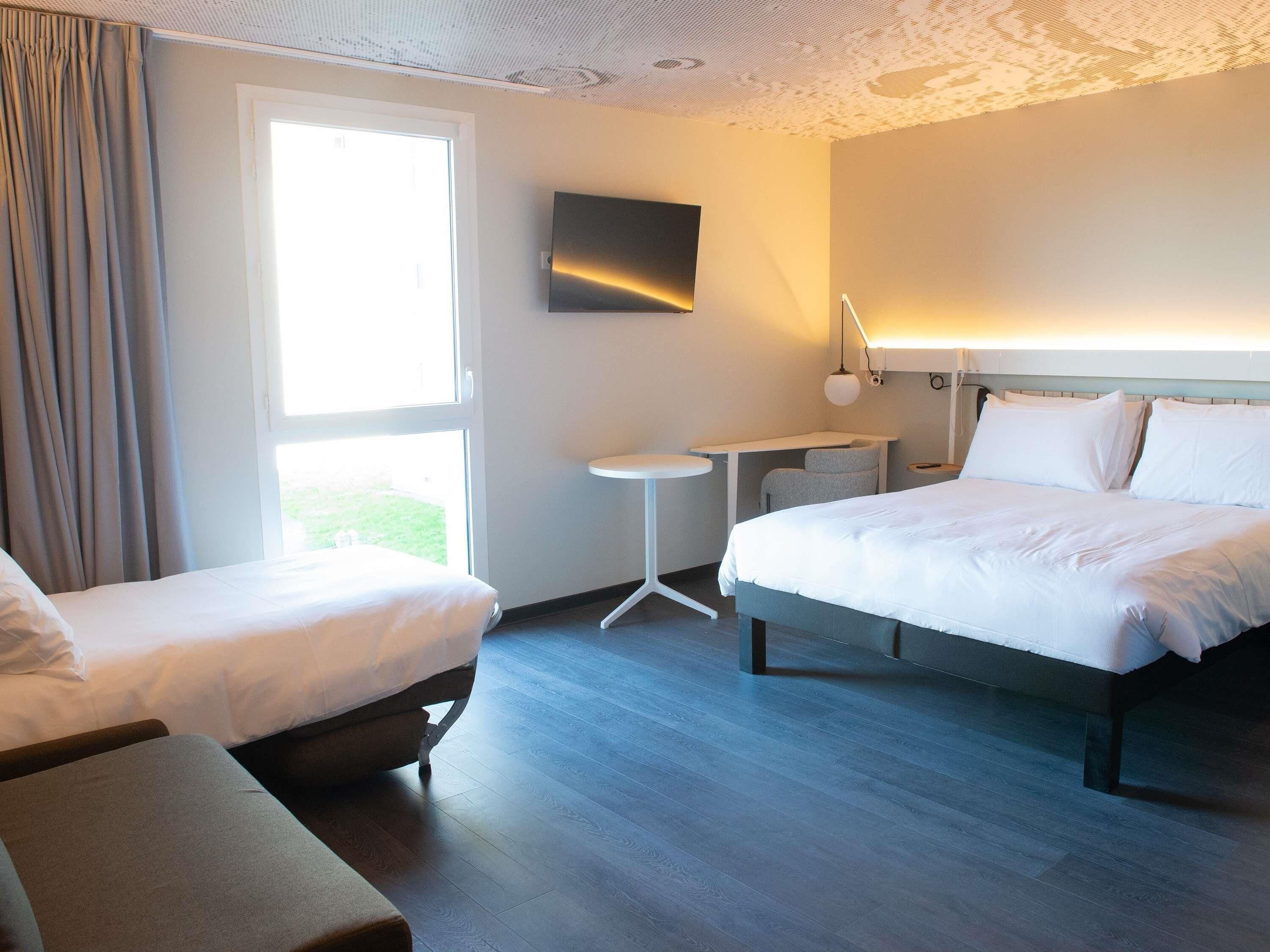 A hotel room with two beds, a desk, a chair, and a TV.