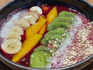 Un saladier rempli d’une salade de fruits contenant des bananes, des mangues, des kiwis et du granola.