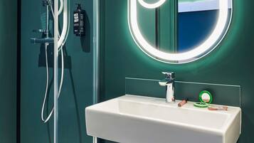 A bathroom with a white sink, a handheld showerhead, a bottle of shampoo, and a mirror with a circular light.