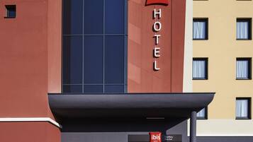Un edificio de hotel moderno con una fachada destacada de color rojo y azul, que muestra el logotipo 'ibis' y la señalización 'HOTEL'.
