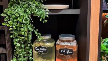 Een plank met twee glazen potten, gelabeld 'Eau Detox CITRON' en 'Thé glace', en een hangende plant.