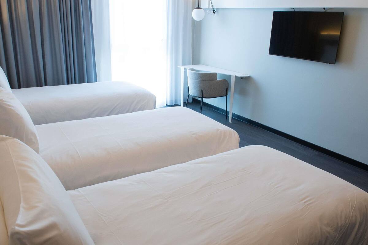 Een hotelkamer met twee bedden, een klein tafeltje, een stoel en een tv aan de muur.