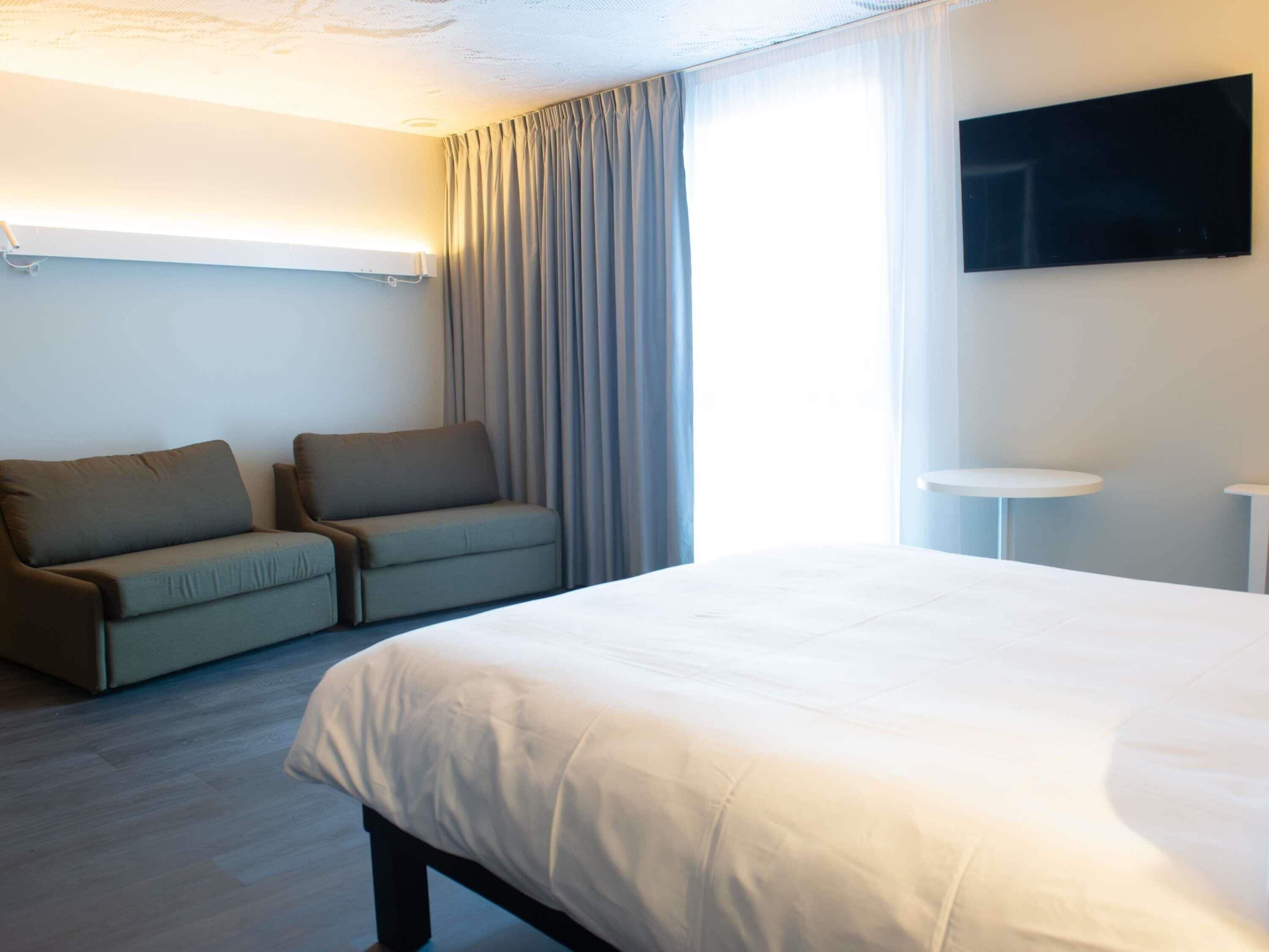 A hotel room with a bed, a sofa, a TV, and a small table.