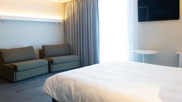 A hotel room with a bed, a sofa, a TV, and a small table.
