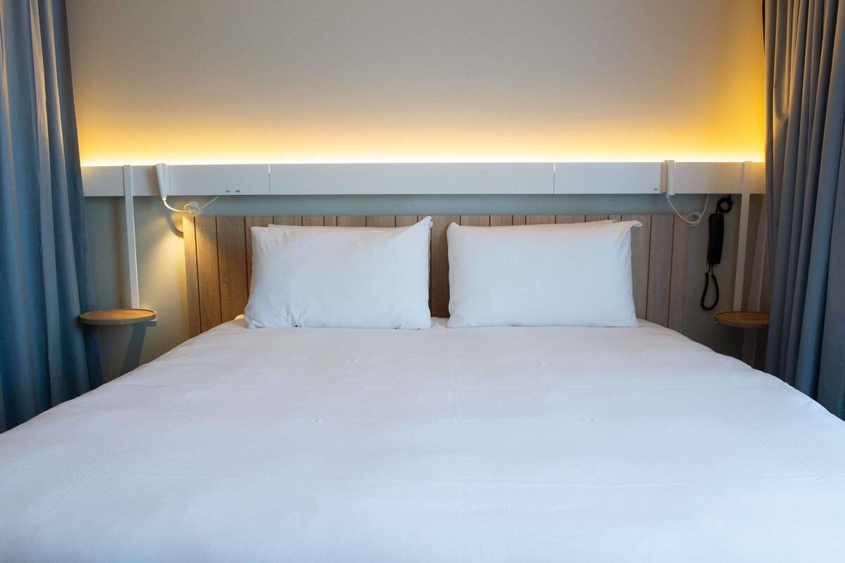 Ein Hotelzimmer mit einem Bett, zwei Nachttischen, einem Telefon und Vorhängen.