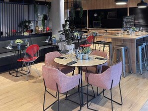 Un restaurant moderne avec des tables rondes, des chaises à armature métallique rouge et un espace bar.