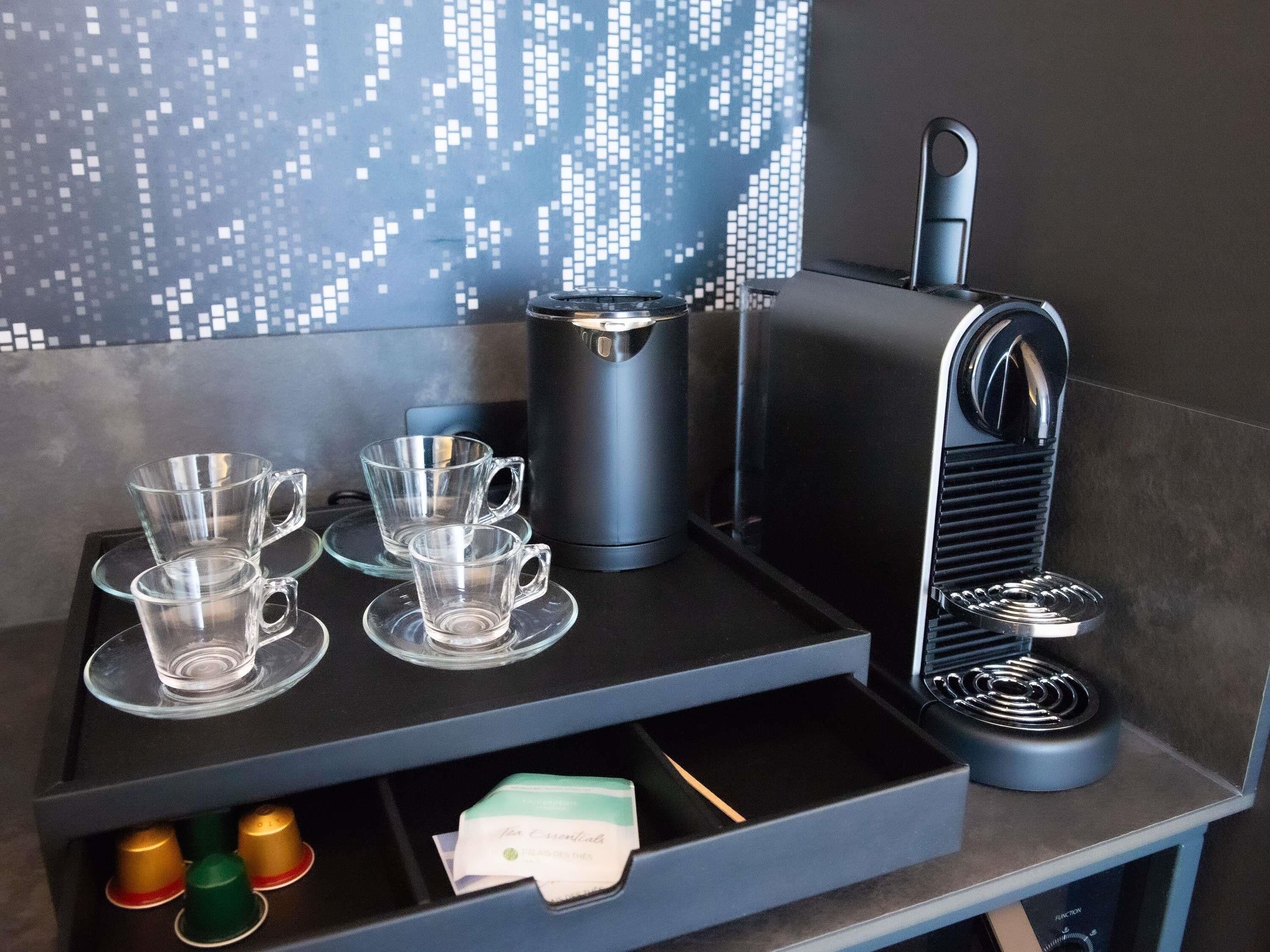Una màquina de cafè amb un pantalla digital, dues tasses de vidre transparent i un compartiment per càpsules de cafè.