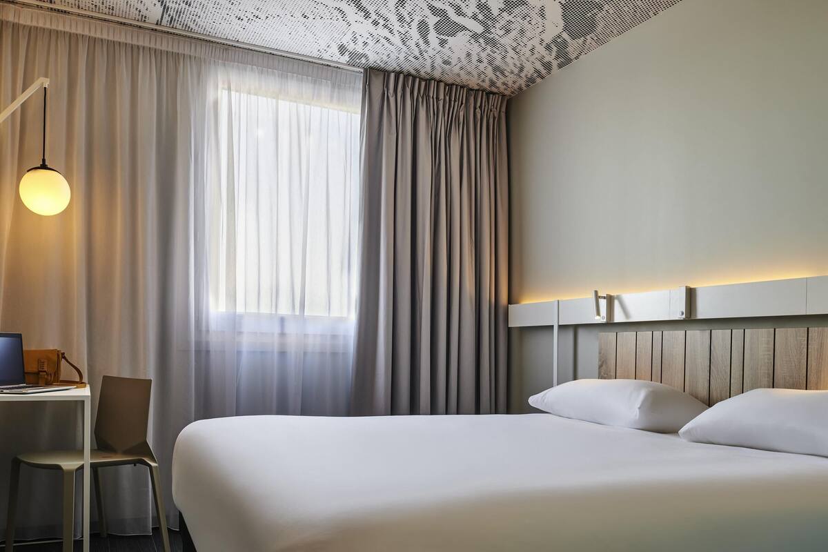Een hotelkamer met een bed, een bureau, een stoel en een raam met gordijnen.
