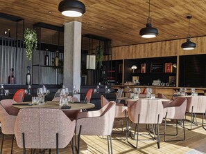 Un interior de restaurante moderno con mesas redondas, sillas acolchadas, iluminación colgante y techo de madera.